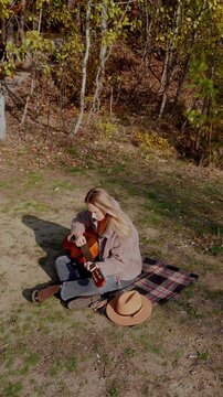 Beautiful blonde girl playing acoustic guitar and singing relaxing enjoying outdoors on sunny autumn day. Hippie woman in boho style learning and practicing playing musical instrument. Fall leaves