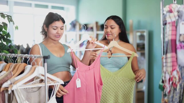 Two girlfriends chooses dresses or o tops for the summer period in a fashionable clothing store. High quality 4k footage