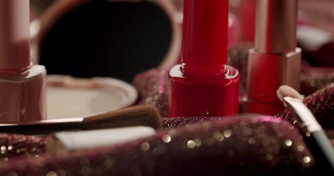 Luxurious decorative cosmetics, including nail polish, lipstick, brushes, and powder, with golden glitter falling in slow motion on a shimmering fabric for a glamorous beauty concept