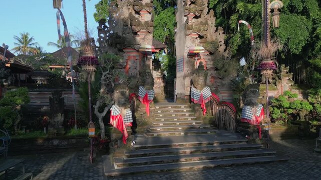 Cinematic FPV drone flight at Balinese Hindu temple with traditional gate, stone statues and ceremonial decorations in Ubud Bali, Indonesia. Cultural and spiritual landmark.