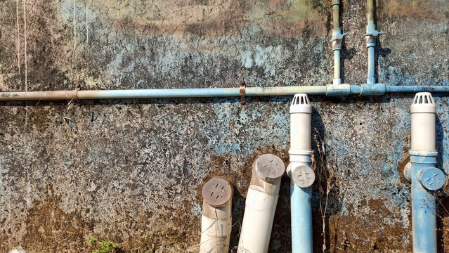 building infrastructure decay, the background has a weathered wall with visible cracks and stains it has several pipes attached, showing signs of aging