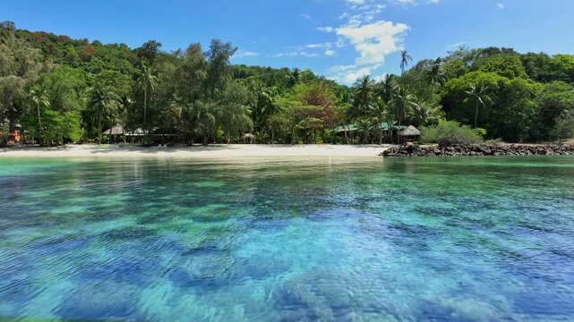 Beautiful tropical beach landscape with white sand, turquoise sea water, and lush green trees under a cloudy blue sky; scenic view of a peaceful island destination for summer vacation and travel conce