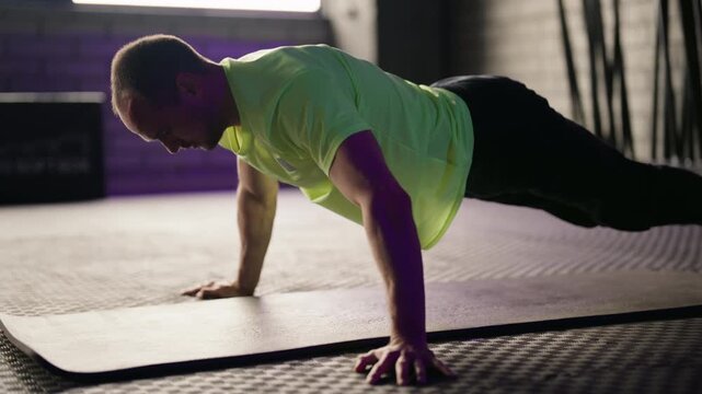 Strong athletic man in sportswear doing push-ups on a mat in a gym. Bodybuilder training strength and endurance with intense fitness exercises, working out his chest and arms