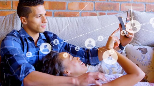 Profile icons connecting with lines over multiracial couple taking selfie with smartphone on sofa