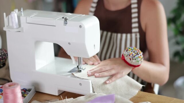 Female hands sewing fabric on a sewing machine in close-up. Seamstress working in a workshop and making a seam on textiles. High quality 4k footage