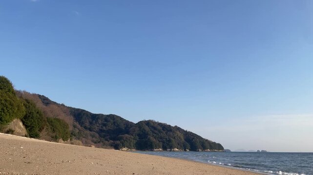 A calm coastal scene in the Seto Inland Sea, Japan. Gentle waves move quietly under soft natural light, with a peaceful island landscape in the distance. The atmosphere is still and minimal, capturing