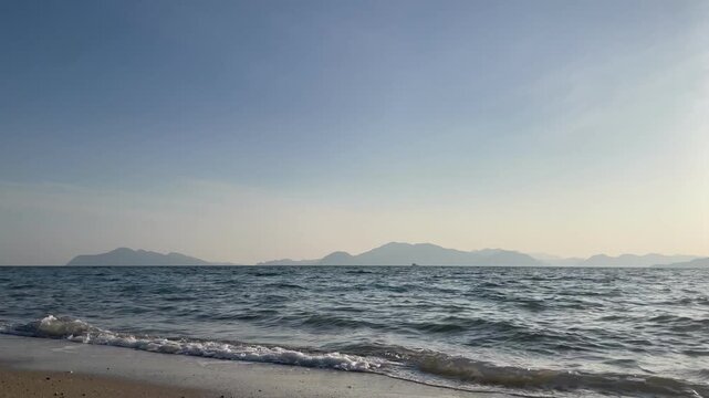 A calm coastal scene in the Seto Inland Sea, Japan. Gentle waves move quietly under soft natural light, with a peaceful island landscape in the distance. The atmosphere is still and minimal, capturing