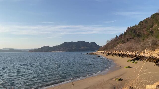 A calm coastal scene in the Seto Inland Sea, Japan. Gentle waves move quietly under soft natural light, with a peaceful island landscape in the distance. The atmosphere is still and minimal, capturing