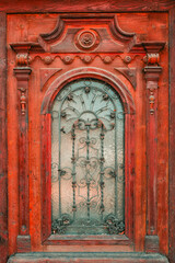 Antique red-painted wooden door featuring elaborate carved baroque frame with central rosette, scrollwork, decorative corbels, turned pilasters and spherical finials © Bits and Splits
