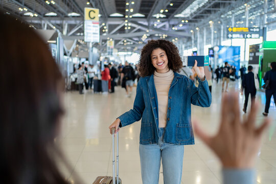 Latina woman happily waving to greet her friend in the airport terminal. 