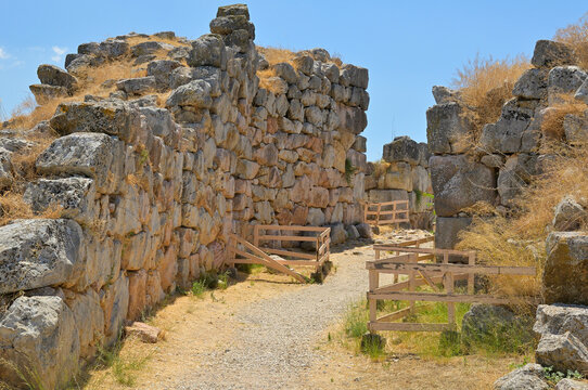 Tiryns ancient cyclopean walls on a sunny day. Ancient Mycenaean cyclopean walls defining an archaeological pathway under a blue sky.