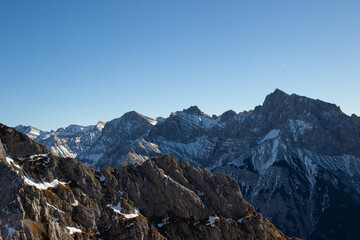 Snow-capped mountain peaks under clear blue sky, showcasing rugged terrain and rocky slopes in the background of a breathtaking alpine landscape