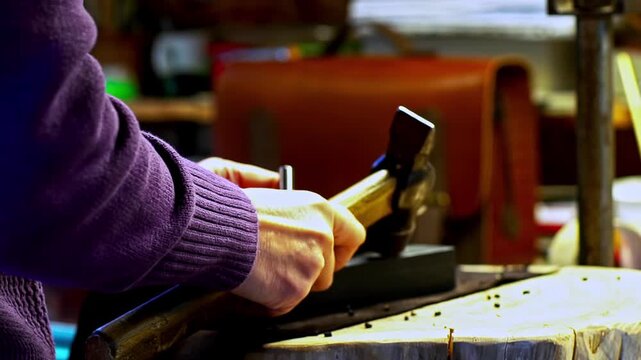 Close up of artisan hands crafting leather with a hammer in workshops