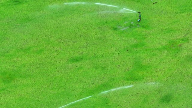 Drone view of a sprinkler watering grass under bright conditions, symbolizing eco-conscious landscaping, optimized irrigation planning, and healthy turf sustainability.
