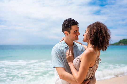 Caucasian young man hugging his Latina girlfriend on a sandy beach. 