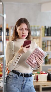 Girl scan QR-code on raw pork sausages package in store. Market visitor choose consider raw pork sausages semi finished products. Buyer pick up meat ware for bbq