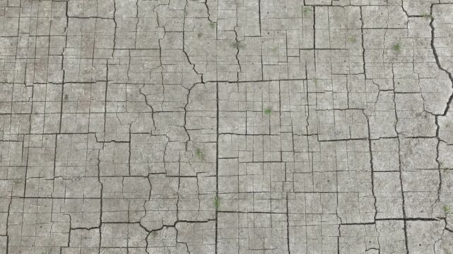 Drone perspective of dry, fragmented ground with visible cracking, representing prolonged drought conditions, reduced soil moisture, and ecological imbalance.

