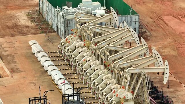 High-angle drone shot of oil pump units aligned in production, symbolizing large-scale petroleum output, market instability, and the continued importance of oil in global energy transitions.
