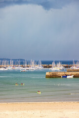 Fototapeta premium Canoes in the sea at a sandy beach and a pier with a marina