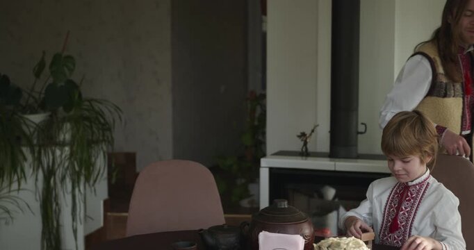 Kid Boy Waiting For Dinner. Man Serving Dishes on Table Family in Ukrainian Traditional Attire Childhood. 4K 10-bit