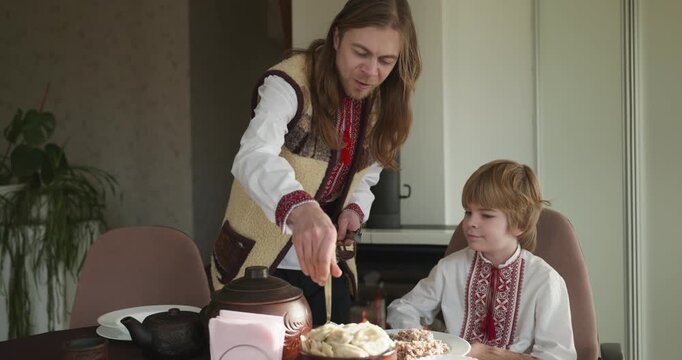 Kid Boy Waiting For Dinner. Man Serving Dishes on Table Family in Ukrainian Traditional Attire Childhood. 4K 10-bit