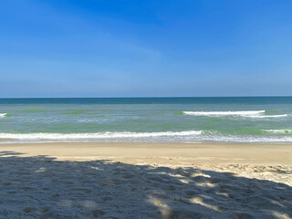 Fototapeta premium Tranquil beach with gentle waves, clear sky, and soft sand in bright sunlight.