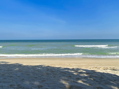 Tranquil beach with gentle waves, clear sky, and soft sand in bright sunlight.