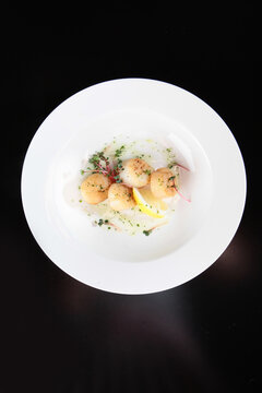Scallops on a white plate with microgreens. Seafood dish. A slice of lemon and scallops. Healthy food. Low-calorie food. Flat lay. Top view. Copy space. Black background.
