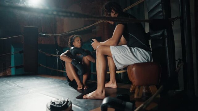Athletic african man and woman resting after hard box workout, sitting on ring. Sport activity in fitness club for keep fit and stay slender, positive emotions and endorphins release by sport