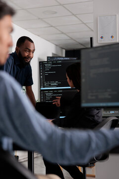 Multi ethnic team of software developers talking about html code in it company office. Artificial intelligence cloud programers compiling algorithms on terminal window server, doing teamwork