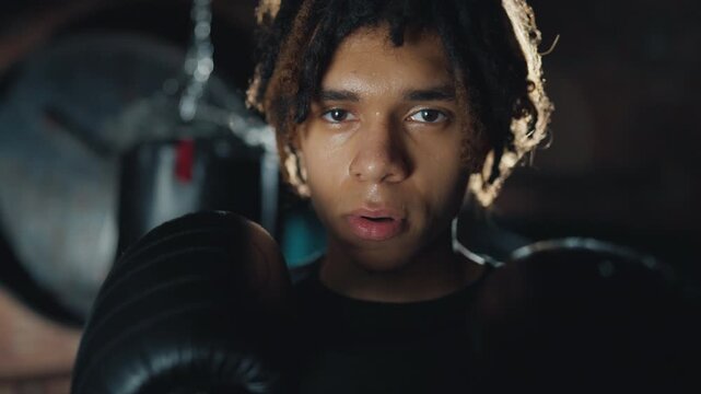 Calm and self-confident face of male boxer fighter, guy holding hands in gloves. Motivated or tired sportsman after fight or workout in gym, active sport exercises in fight club, be brave and strong