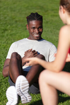 man doing sit-ups in the park encouraged by female trainer