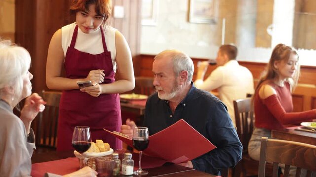 Young woman waitress takes order from couple elderly man and elderly woman in restaurant