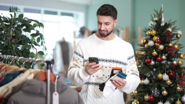 Man scans QR code and label of socks using mobile phone camera, X mas shopping. Customer client is interested in country of origin of product, checks certificate on consumer protection website