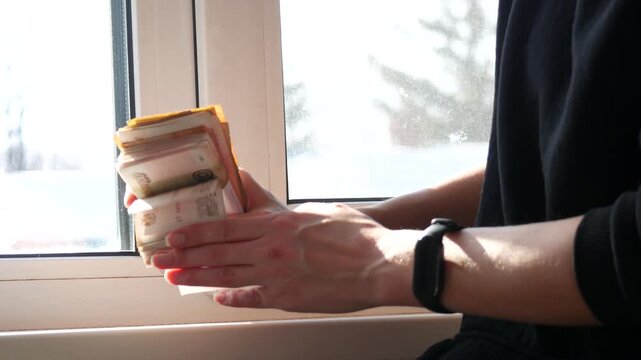 Woman holding stack of money banknotes near bright window. Person counting cash savings, financial planning and success concept. Wealth investment economy routine.