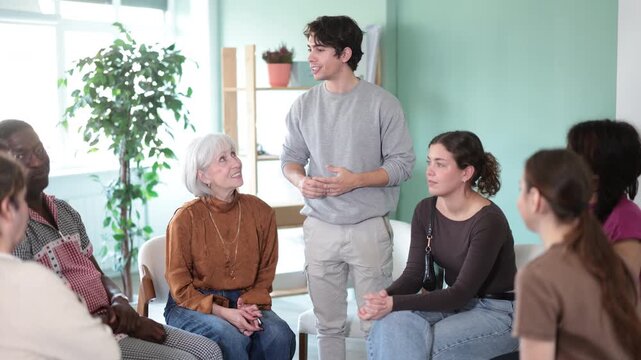 Emotional young man talking to colleagues gathered in circle in office rest room, sharing personal stories during work break. High quality 4k footage