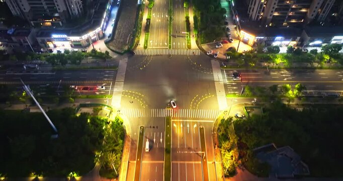Top view of bridge illuminated by warm streetlights at night, showing urban traffic crossing a calm river in a city park setting with lush green trees and pedestrian paths.
