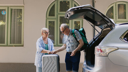 Retired couple loading voyage luggage in car trunk while going on marriage anniversary summer...