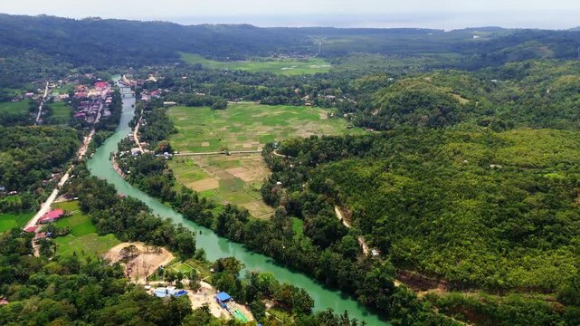 Wide aerial perspective of the Loboc River valley in Bohol, Philippines. Featuring the emerald river surrounded by dense tropical forests, mountains, and traditional rural farmlands
