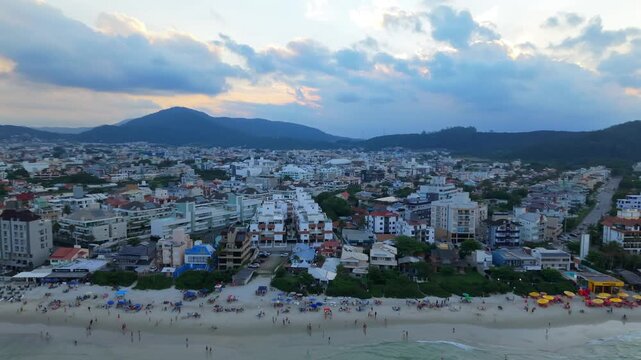 Aerial recede pull back passing over residential houses, beach sand, and bathing tourists at Praia dos Ingleses, Santa Catarina, Brazil.