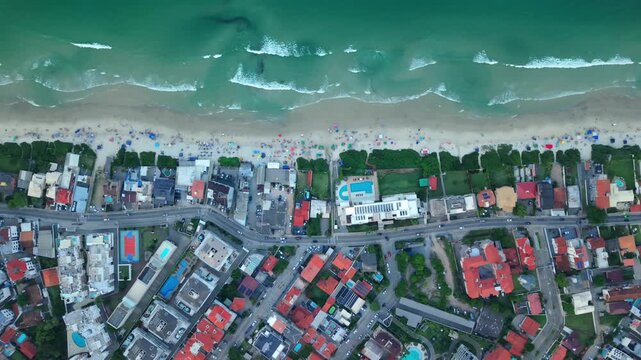 Residential neighborhood, sandy beach, and breaking turquoise waves at Praia dos Ingleses, Santa Catarina, Brazil. Top down forward aerial pass.