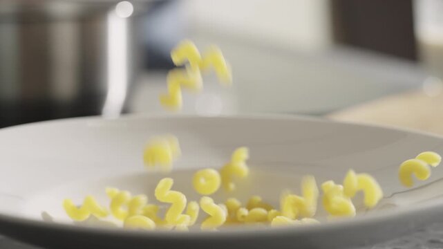 Slow motion dried cellentani pasta fall into plate closeup