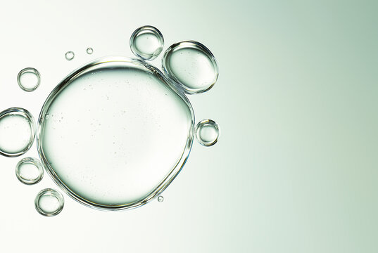 Macro view of a large clear liquid bubble with micro droplets on a pale mint green background