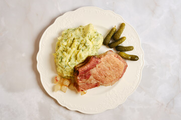 Enjoying a pork rib chop meal with mashed potatoes and pickles on a white plate © boomeart