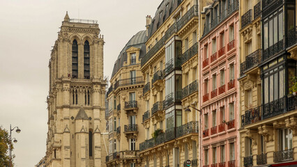 Obraz premium Notre Dame de Paris cathedral tower rising above classic Haussmannian apartment buildings on a city street in France