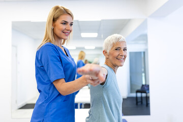 Obraz premium Senior woman performing arm stretching exercises with a physiotherapist. Physical therapy for shoulder mobility in a modern clinic. Healthcare and medicine concept. Elderly patient rehabilitation.