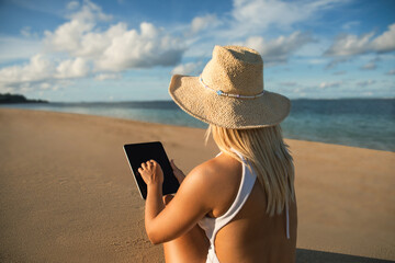 Fototapeta premium Person using a tablet by the water on a sandy beach
