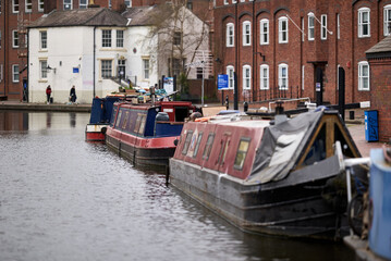 Obraz premium Row of narrowboats moored along the Birmingham Canal Navigations in front of red brick residential buildings, Birmingham, West Midlands, England, UK.
