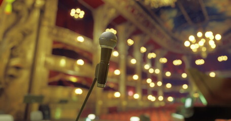 A microphone stands prominently in a beautifully lit theater with chandeliers, signaling the anticipation of a live performance as the audience prepares for an entertaining evening. © icetray