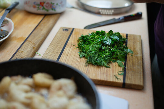 Food is cooked on the stove, chopped parsley, dill and other greens in a pile are on the table. Authentic Photo Cooking DMA
